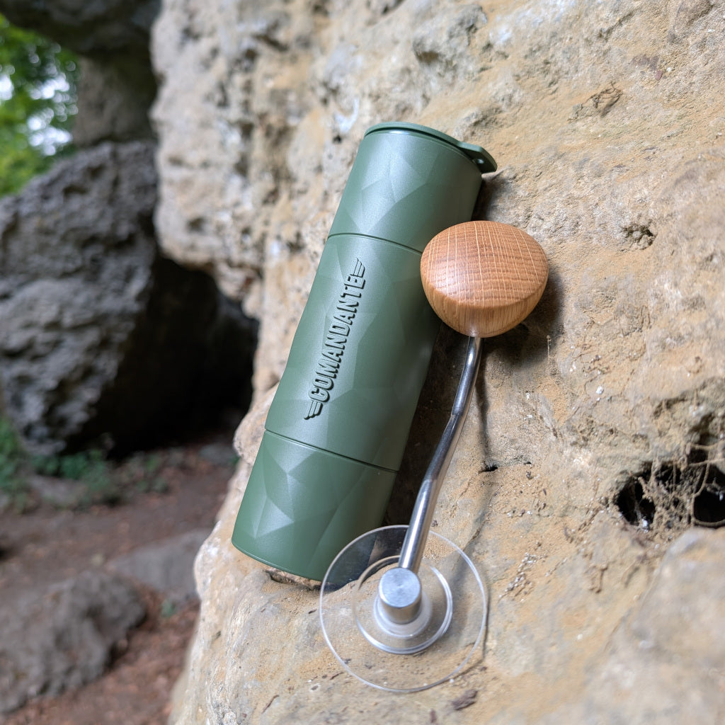Das Bild zeigt eine grüne Comandante Handmühle mit Kurbel, angelehnt an eine Felswand und im Hintergrund einen Felsvorsprung der überhängend darüber zeigt.
