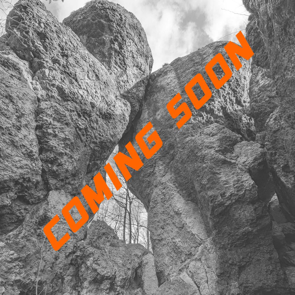 Das Bild zeigt im Hintergrund Felsformationen die wie Türme aussehen und ein Tor Bilden in schwarz weiß. Die Strucktur der Felsen ist rau. Im Bild quer findet sich eine orangene Schrift welche - COMING SOON - aussagt.