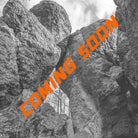 Das Bild zeigt im Hintergrund Felsformationen die wie Türme aussehen und ein Tor Bilden in schwarz weiß. Die Strucktur der Felsen ist rau. Im Bild quer findet sich eine orangene Schrift welche - COMING SOON - aussagt.